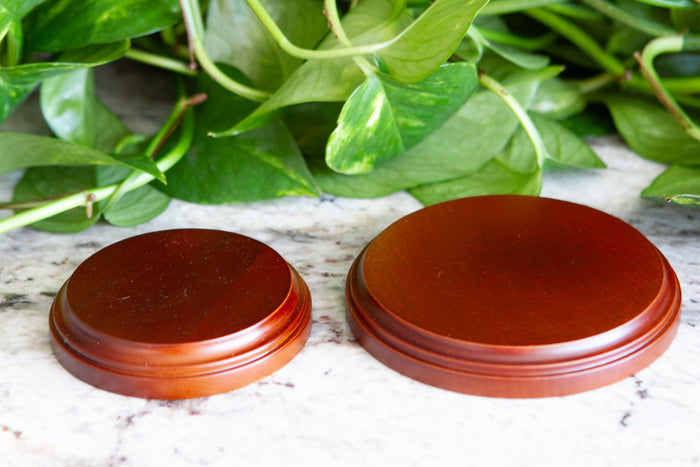 Two circular wooden stands on a marble surface with green leaves in the background