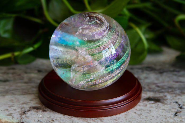 Dichroic rainbow orb on a circular wooden stand with iridescent bands