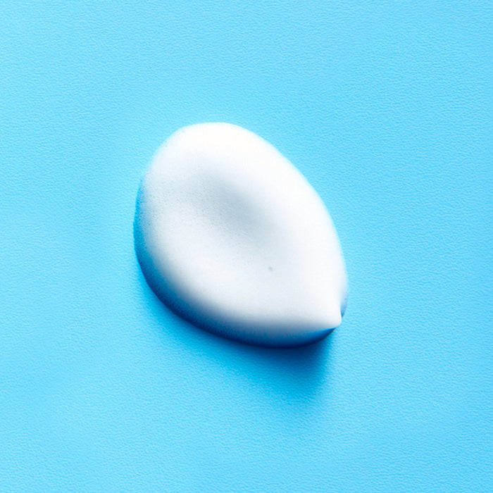 A dollop of CLEANSE ME Foaming Micellar Water by FRÉ Skincare, with its white foam, sits on a smooth, bright blue surface.