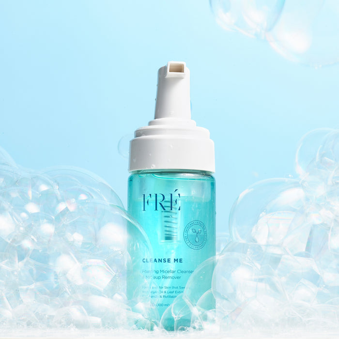 A bottle of FRÉ Skincare CLEANSE ME Foaming Micellar Water, a gentle facial cleanser and makeup remover, stands upright among white bubbles on a light blue background.