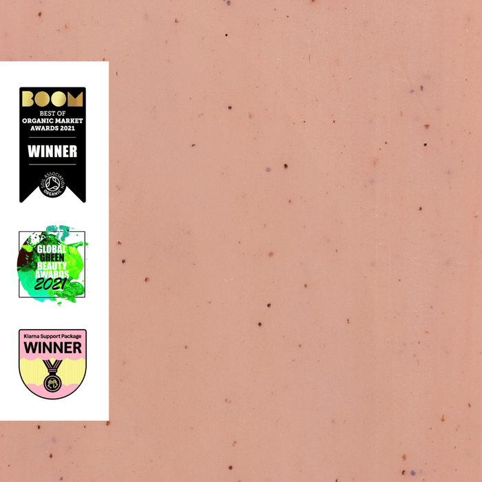 A pink background with small dark specks features three award badges on the left: a black "Best of Organic Market Awards 2021" badge, a green "Global Green Beauty Awards 2021" badge, and a pink "Winner" badge with a medal design.