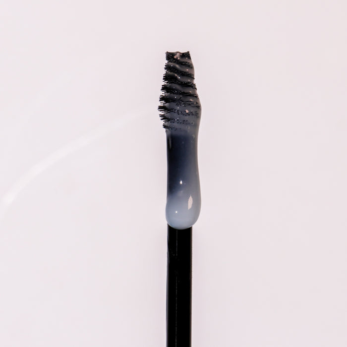 A close-up shows the Clear Avocado Brow Gel with Castor Oil by Everyday For Future. The evenly spaced black mascara wands bristles hold a droplet of its vegan, cruelty-free formula, enriched with nourishing organic avocado oil, glistening against a white background.