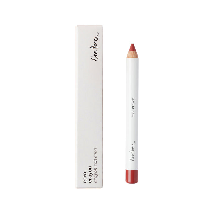 The Ere Perez Coco Crayon, a red lip crayon with a white barrel and wooden tip, is displayed next to its matching white box. This natural beauty product boasts an elegant, hydrating creamy formula ideal for eco-conscious makeup enthusiasts.