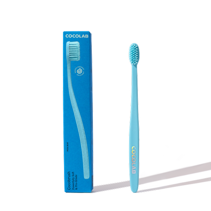 A blue Cocobrush Toothbrush by COCOLAB with soft bristles stands upright beside its matching blue box, which displays the toothbrush image and the COCOLAB brand name in white text.