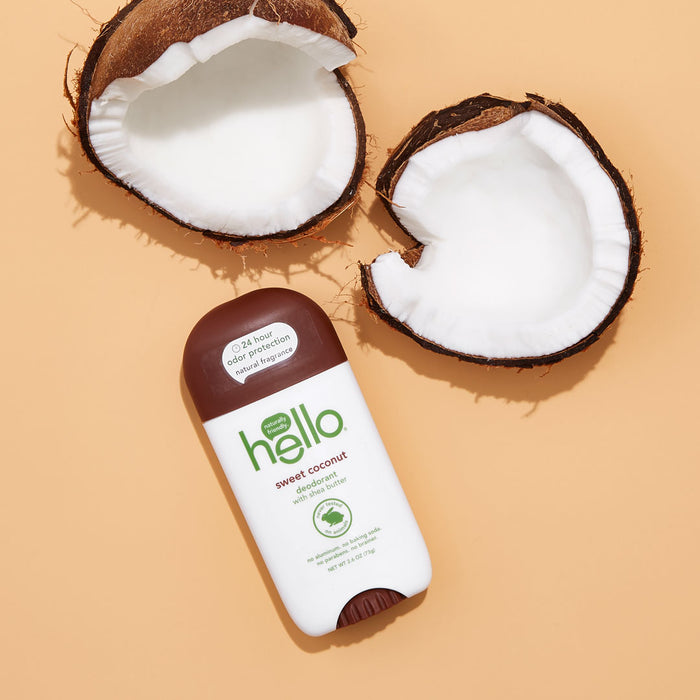 The hello Coconut Deodorant with Shea Butter features a brown cap and green text on a stick surrounded by cracked coconuts on a peach background, highlighting its vegan, cruelty-free essence.