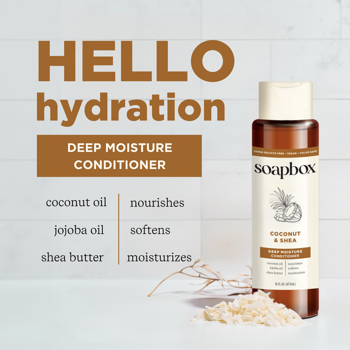A bottle of Soapbox Coconut & Shea Deep Moisture Conditioner is shown, highlighting ingredients like coconut oil, jojoba oil, and shea butter for their nourishing, softening, and moisturizing benefits. The background features pieces of coconut.