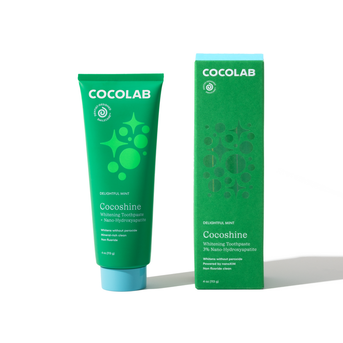 A green tube and matching box of COCOLAB Cocoshine Whitening Toothpaste in Delightful Mint, with white and dark green text and circular designs, stands on a white surface. This fluoride-free toothpaste helps strengthen enamel.
