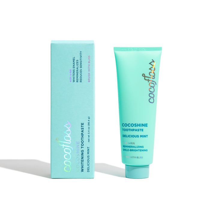A tube and box of Cocoshine Whitening Toothpaste by Cocofloss in Delicious Mint flavor, featuring enamel strengthening with a fluoride alternative, comes in light blue packaging with colorful typography and a smile-brightening nano-hydroxyapatite formula.