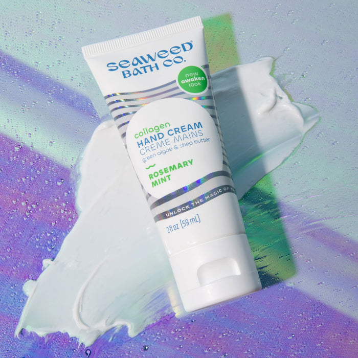 A tube of The Seaweed Bath Co Collagen Hand Cream in rosemary mint is showcased on a cream swirl with an iridescent backdrop, highlighting bio-mimicking collagen and key ingredients like green algae and shea butter for healthy-looking skin.