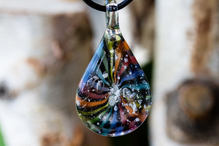 Teardrop glass pendant infused with cremation ashes featuring a rainbow color wheel swirl on a black cord