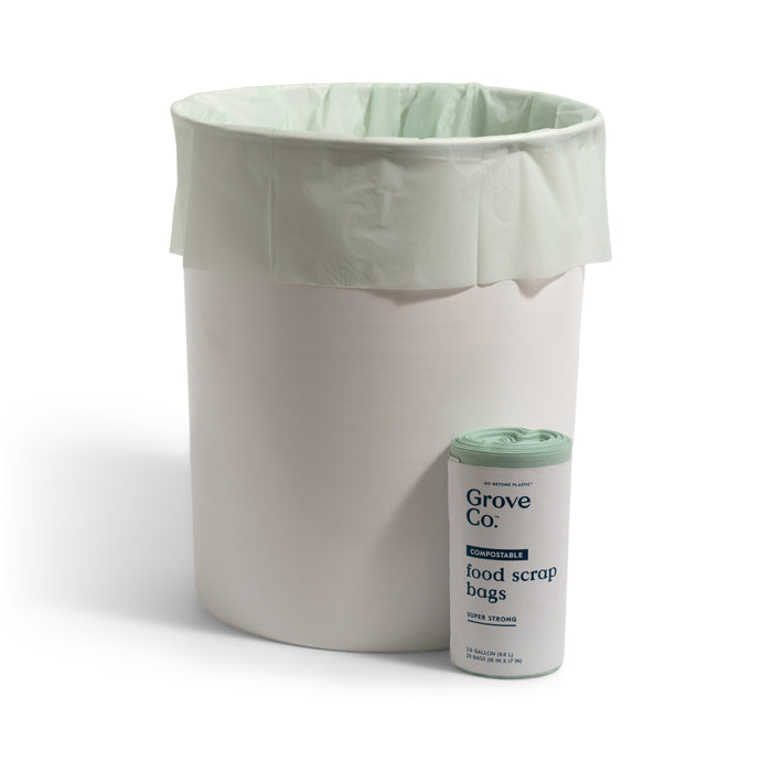 A white trash bin with a light green Grove Co. Compostable Food Scrap Bag stands beside a rolled-up package of the same bags, providing an easy WasteZero solution for eco-friendly disposal.