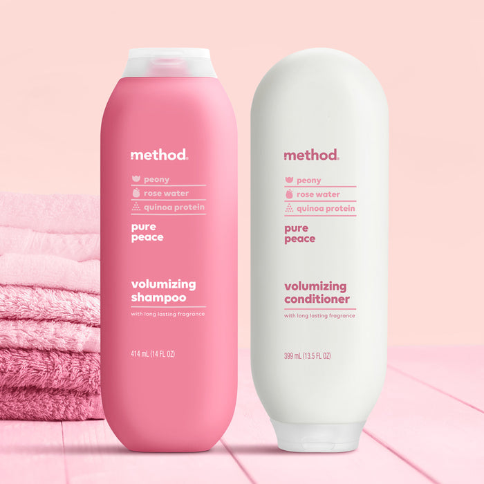 Two bottles of Method Pure Peace hair care products on a pink surface: a vibrant pink bottle of volumizing shampoo and a sleek white conditioner, both cruelty-free with peony, rose water, and quinoa protein in recycled plastic bottles. Pink towels act as the backdrop.