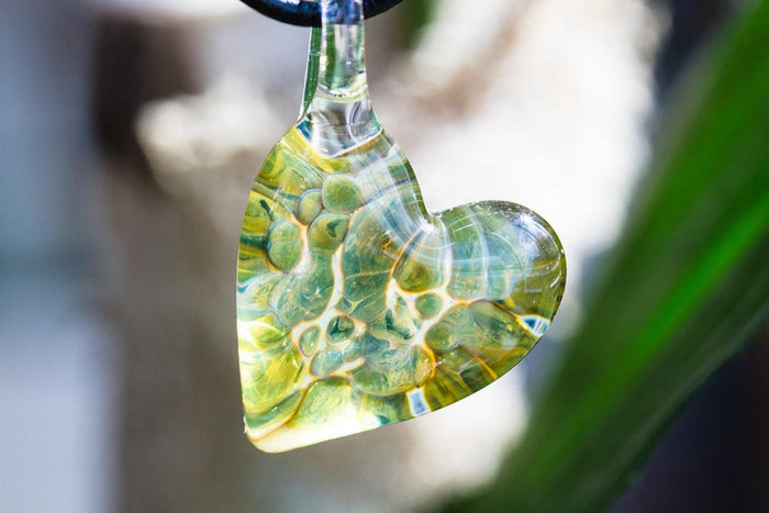 Close-up of a green glass heart pendant with blue specks infused with cremation ashes.