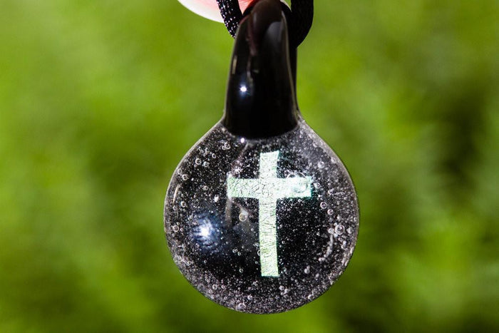 Round glass cremation ash pendant with a holographic cross inside, suspended from a cord.