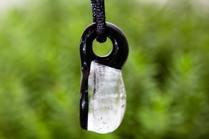 Front view of round glass ash pendant with holographic cross, suspended from a black cord.