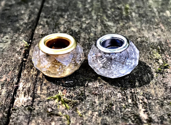 Two faceted crystal beads with gold and silver cores resting on a weathered wood surface