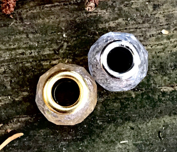Two crystal-cut cremains beads with gold and silver inner rims on a weathered wooden surface.