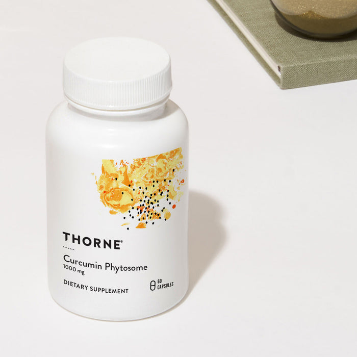 A white bottle labeled Thorne Curcumin Phytosome with abstract yellow-orange designs is on a light surface, promoting curcumin support for healthy inflammatory response. It contains 60 capsules. A tray with objects is partially visible at the top right.