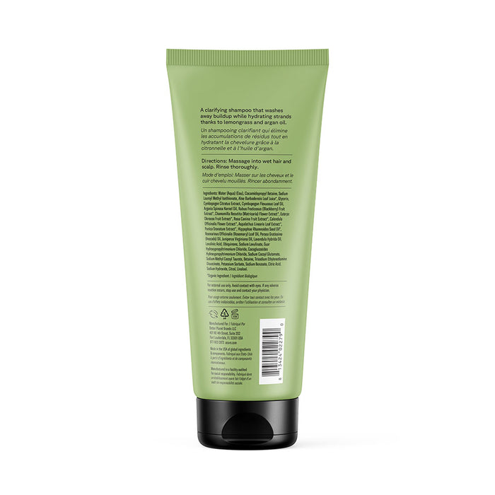 A green tube of Acure Curiously Clarifying Shampoo with a black flip cap is shown from the back. The packaging displays product info, instructions, and lemongrass ingredients in white text, plus a barcode and recycling symbols at the bottom.