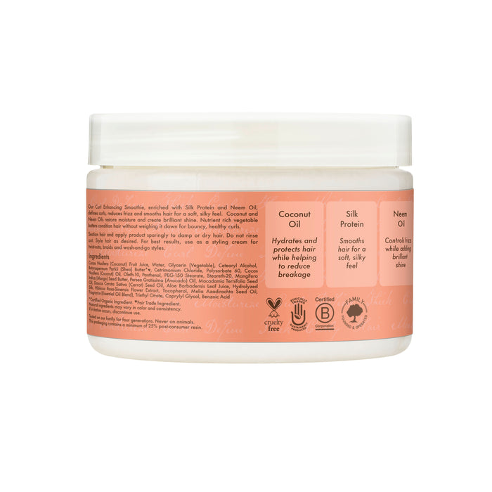 A jar of SheaMoisture Styling Aid Smoothie Curl Enhancing, featuring a peach-colored label with listed ingredients and benefits. This product claims to hydrate, protect, reduce breakage, smoothen, and add shine—making it an ideal anti-frizz solution for curly hair. Symbols on the package indicate that it is cruelty-free, clean beauty certified, and vegan. Inspired by favorites like the SheaMoisture Coconut & Hibiscus Curl Enhancing Smoothie, this curl enhancing smoothie delivers beautiful definition with