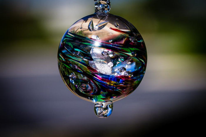 Dark confetti glass orb containing cremation ashes with jewel toned swirls and a hanging loop at the bottom