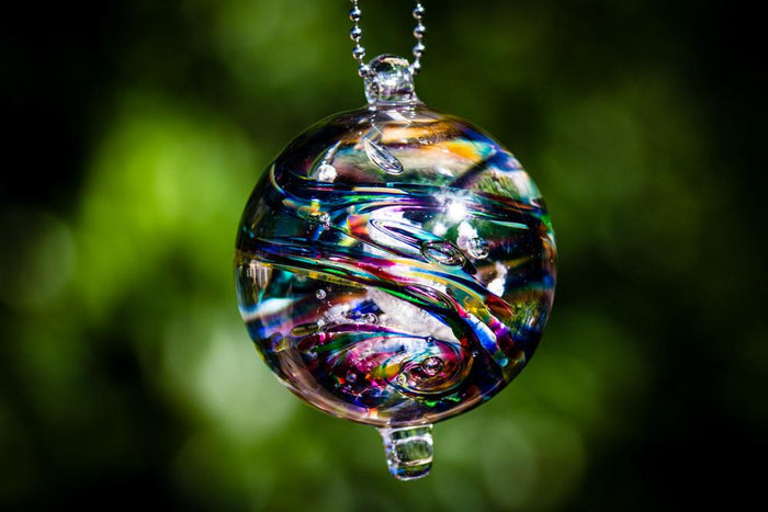 Dark confetti glass orb with embedded cremation ashes and jewel-toned swirls hanging from a metal bead chain.