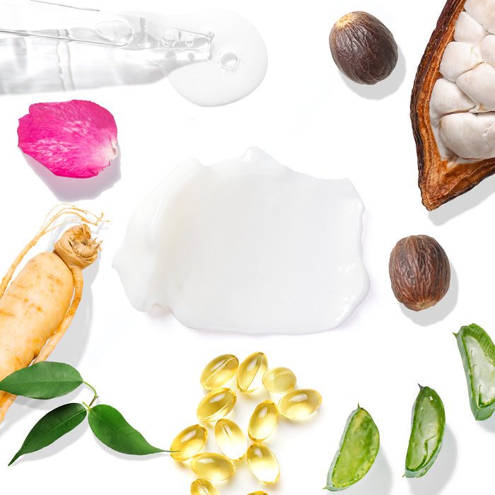 Flat lay of skincare essentials: ginseng root, rose petal, aloe vera pieces, yellow capsules, leaves, nutmeg seeds, a nutmeg half, and a clear liquid with dropper on white background—vital ingredients in Tree To Tubs Deep Hydrating Moisturizer for Sensitive Skin with Green Tea.
