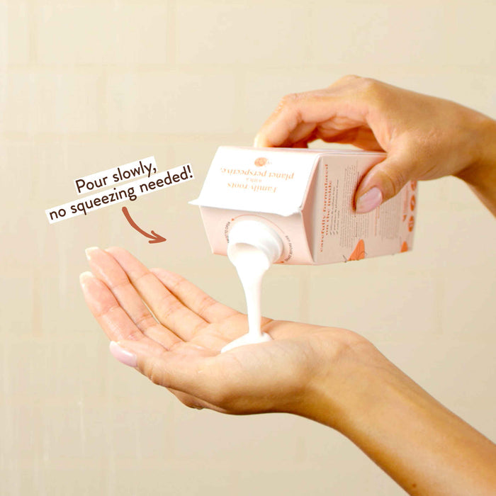 Hands pouring creamy white liquid from a carton labeled "Pour slowly, no squeezing needed!" into an open palm. The carton design suggests it contains a personal care product.