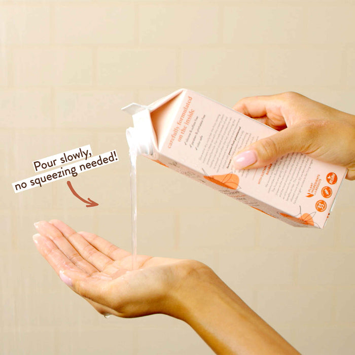A person is pouring a liquid from a carton into their cupped hand. The carton has a spout at the top, and there's text saying, "Pour slowly, no squeezing needed!" The background is a neutral beige color.