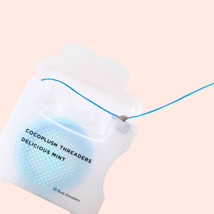 The Cocofloss Dental Floss + Threaders in Delicious Mint features a blue threader against a light pink background and includes 30 floss-and-threader combos, combining chic style with effective dental care.