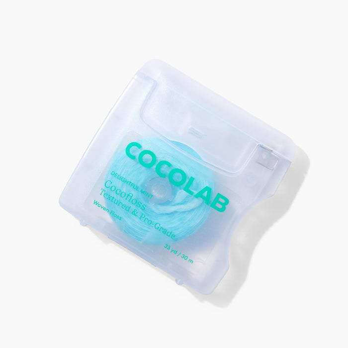 A translucent plastic container of COCOLAB Dental Floss displays textured mint floss inside. The square container with rounded edges features teal text on the front, offering a fresh and eco-friendly approach to plaque removal.