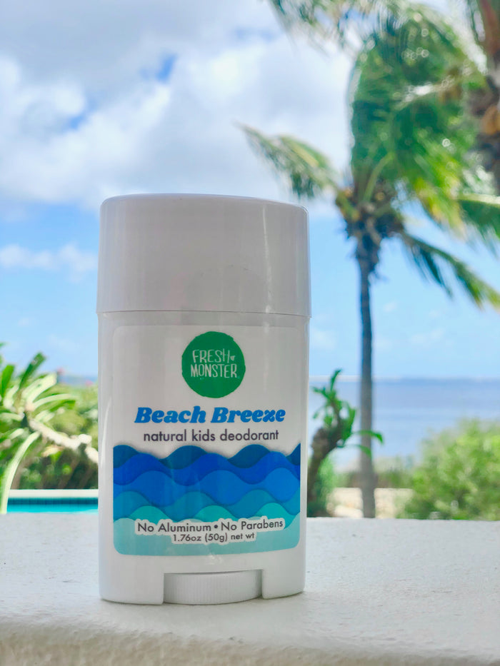 A stick of Fresh Monster Deodorant for Kids and Teens rests outdoors, sporting its No Aluminum, No Parabens label. Its surrounded by palm trees, a pool, and the ocean under a partly cloudy sky—an ideal natural deodorant choice for kids.
