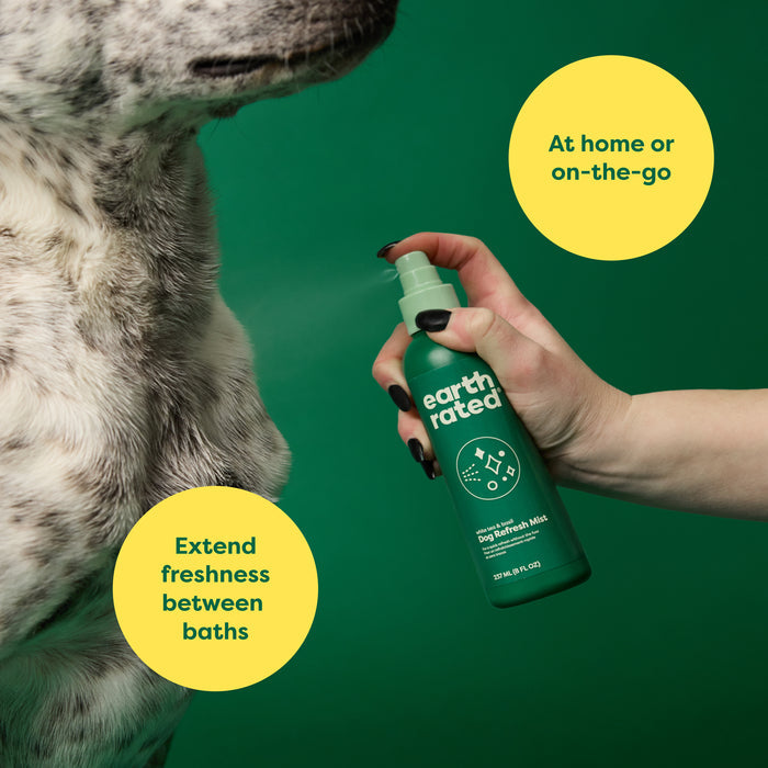A hand with black nails uses a green bottle of Earth Rateds Deodorizing & Conditioning Refresh Mist for Dogs. A dog is partially visible on the left. Yellow circles read: “At home or on-the-go” and “Extend freshness between baths.” This no-rinse solution is a grooming essential.