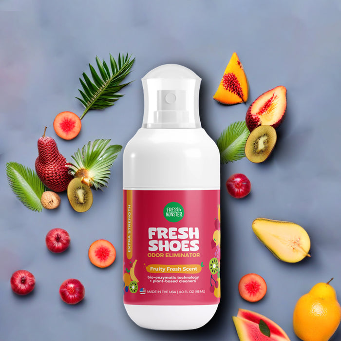 A bottle of Fresh Monster Deodorizing Shoe Spray is showcased on a gray background with colorful fruits and leaves. The label features fruit graphics and promotes its plant-based, bio-enzymatic technology for effective odor removal.