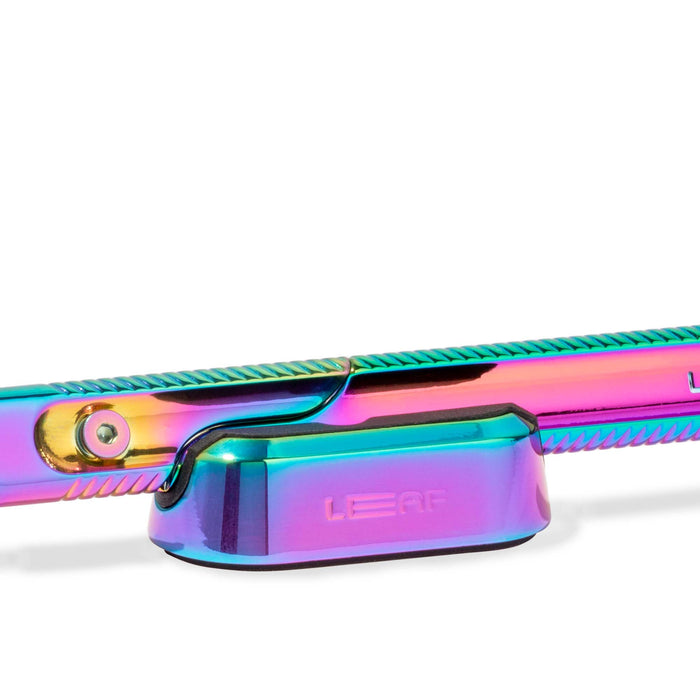 The Leaf Shave Dermaplaner Kit features an iridescent metal razor with a multicolored finish, a smooth elongated handle, and a compact base engraved with Leaf. This zero-waste design adds eco-friendly elegance to your grooming routine.