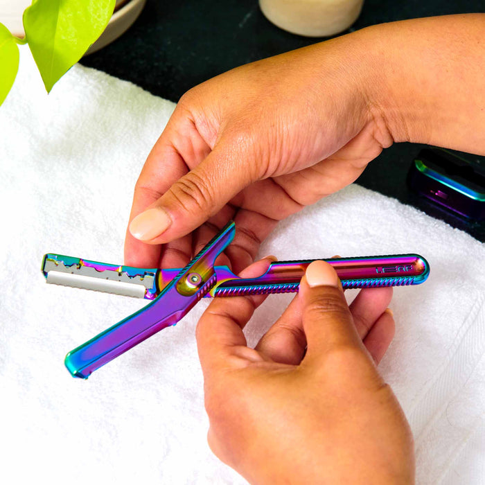 A person is adjusting a Leaf Shave Dermaplaner Kit over a white towel, with a plant in the top left corner. This iridescent, dual-function razor is perfect for zero-waste grooming enthusiasts.