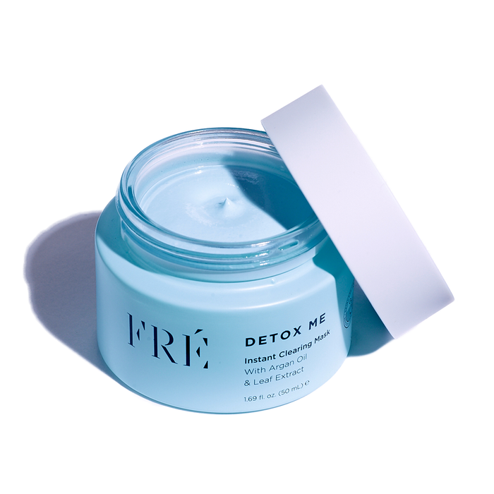 The DETOX ME Instant Clearing Mask by FRÉ Skincare comes in a light blue jar with a white lid, offering a peek at the soothing blue cream. It features argan oil, leaf extract, and kaolin clay for an effective detox experience.