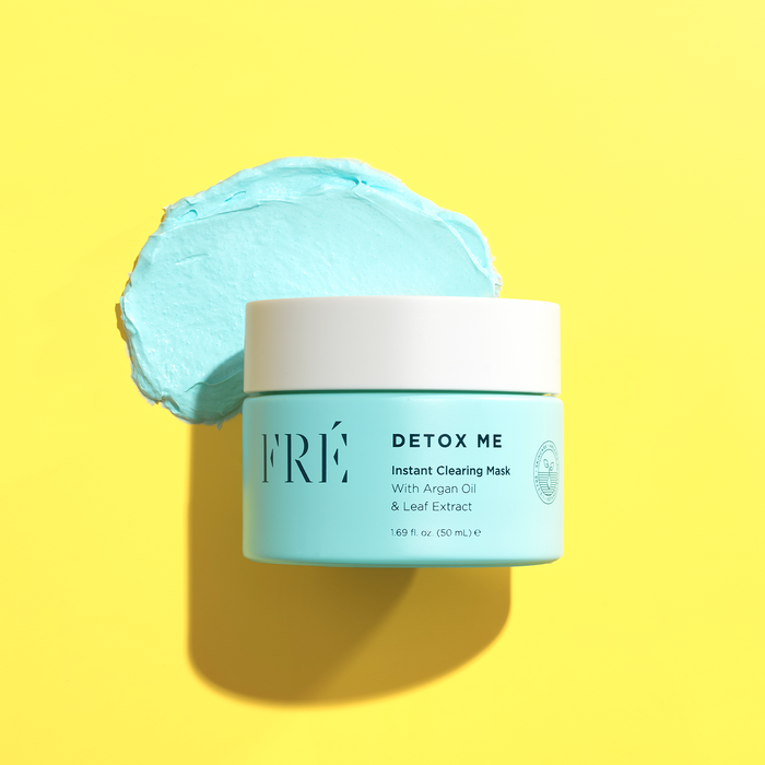 A turquoise jar of DETOX ME Instant Clearing Mask by FRÉ Skincare rests on a bright yellow surface, with a smear of the blue mask behind it. The label showcases argan oil, leaf extract, and natural kaolin clay as main ingredients.