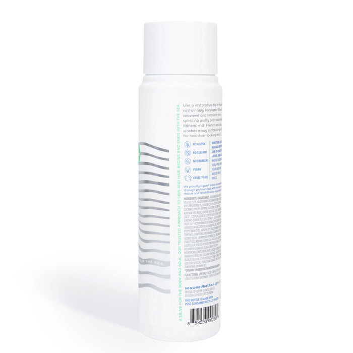 Side view of a cylindrical white bottle with a tall cap featuring a label with text and a wavy line graphic, emphasizing The Seaweed Bath Cos Detox Purifying Body Wash enriched with Green Coffee Bean Extract. The plain white background ensures the focus remains on the product.