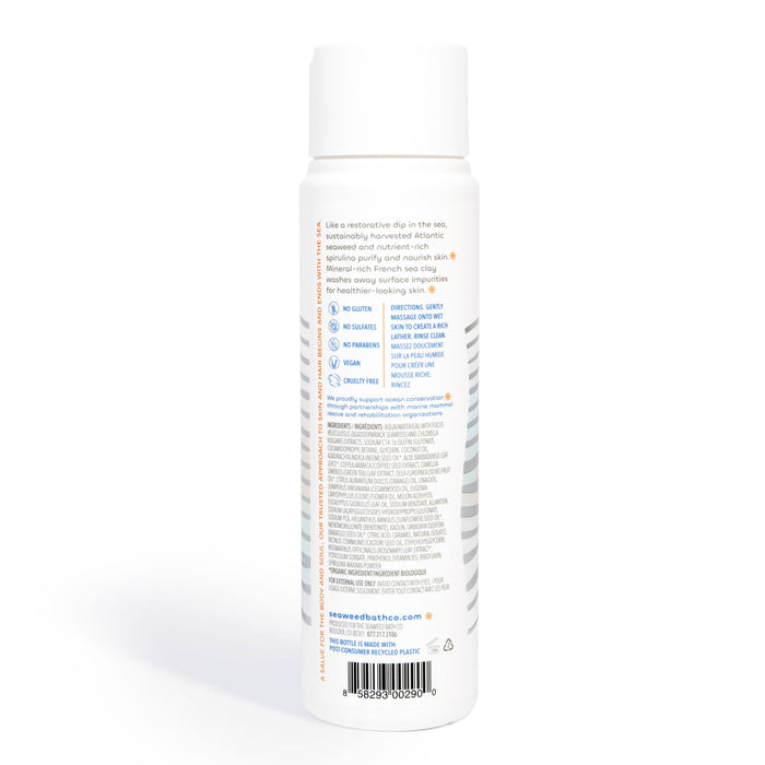 A side-angled view of a cylindrical white bottle from The Seaweed Bath Co displays the Detox Purifying Body Wash label, featuring graphics and text. It includes product details, a bottom barcode, and is topped with a minimalist white lid that exudes purity and simplicity.