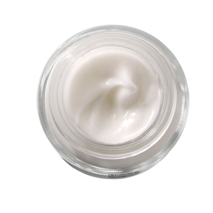 The top-down view of an open Dew Bomb Glowy Hydra-Milk by IZZY Zero Waste Beauty reveals a smooth, glossy surface. Swirls in the center, encased in clear glass, highlight its triple-layer hyaluronic acids rich hydration promise against a simple white backdrop.