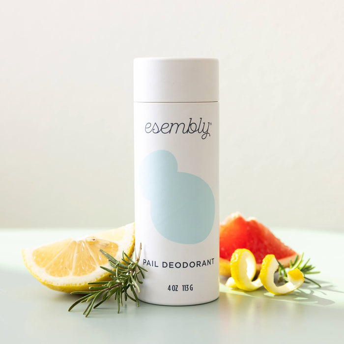An Esembly Baby Diaper Pail Odor Eliminator & Deodorizer sits among rosemary, lemon slices, and grapefruit. This all-natural powder freshens the air against a minimalistic backdrop, exuding a vibe of effortless freshness and nature.