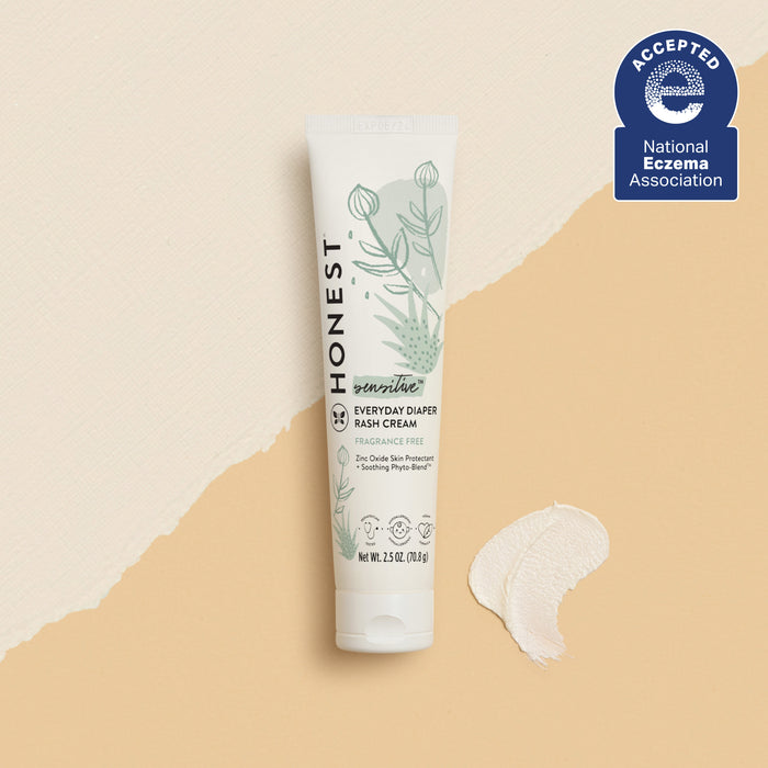A tube of The Honest Companys Diaper Rash Cream, featuring a soothing Phyto-Blend™, is displayed on a neutral background with a dab of hypoallergenic cream. The package showcases botanical illustrations and text, alongside a blue badge indicating its National Eczema Association acceptance.
