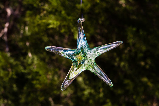 Dichroic glass starfish sun catcher infused with cremains in blue green hues hanging in natural light