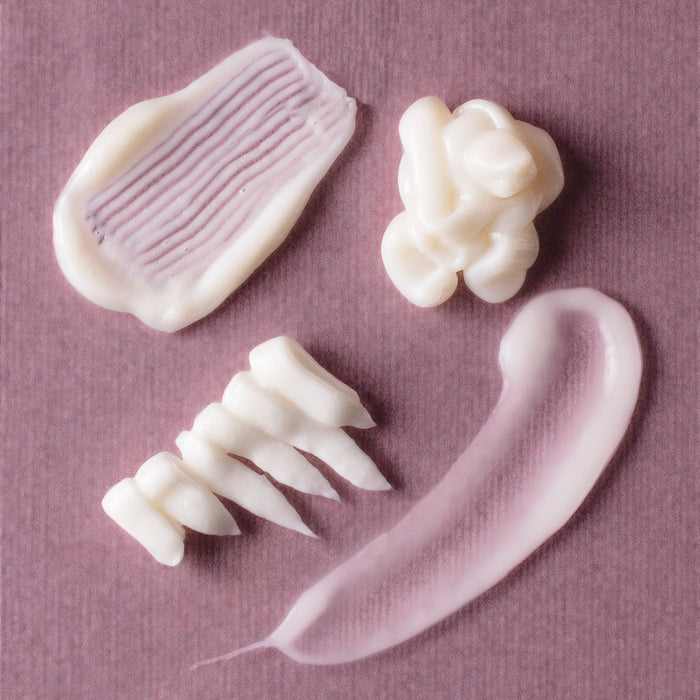 The Holy Curls Discovery Kit creates a visual with samples on mauve. Enjoy diverse textures: a smooth smear, wavy line, gathered dollop, and textured stripe—ideal for refining your Curl Routine.