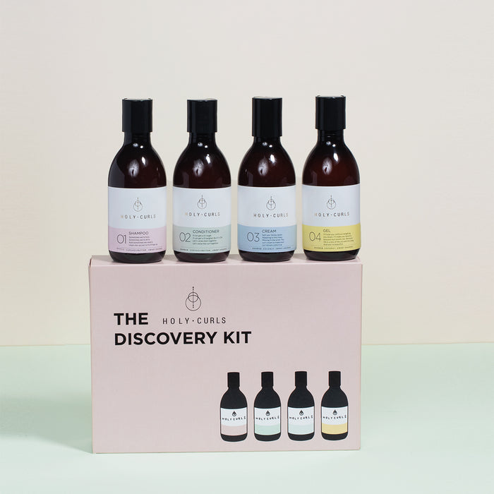 The Discovery Kit by Holy Curls features four hair products with uniquely colored labels, elegantly displayed on a box. The simple, light neutral background highlights the kits essence and enhances your curl routine.