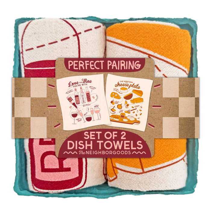 The Neighborgoods Dish Towel Set includes two rolled cotton towels—one red/white, one orange/white—in a carton tray, with wine and cheese illustrations on packaging labeled Perfect Pairing Set of 2 Dish Towel Sets.