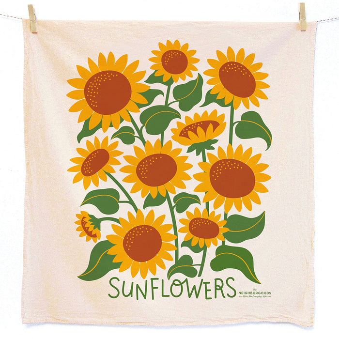 The Neighborgoods Dish Towel showcases vibrant illustrations of sunflowers with lush leaves. Made from unbleached cotton, it brings a natural touch to your kitchen decor. SUNFLOWERS is elegantly printed in green letters at the bottom.