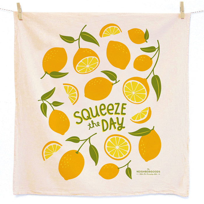The Neighborgoods Dish Towel features absorbent unbleached cotton with bright yellow lemons and green leaves. The phrase Squeeze the Day appears playfully in green, and the towel hangs against a white background.