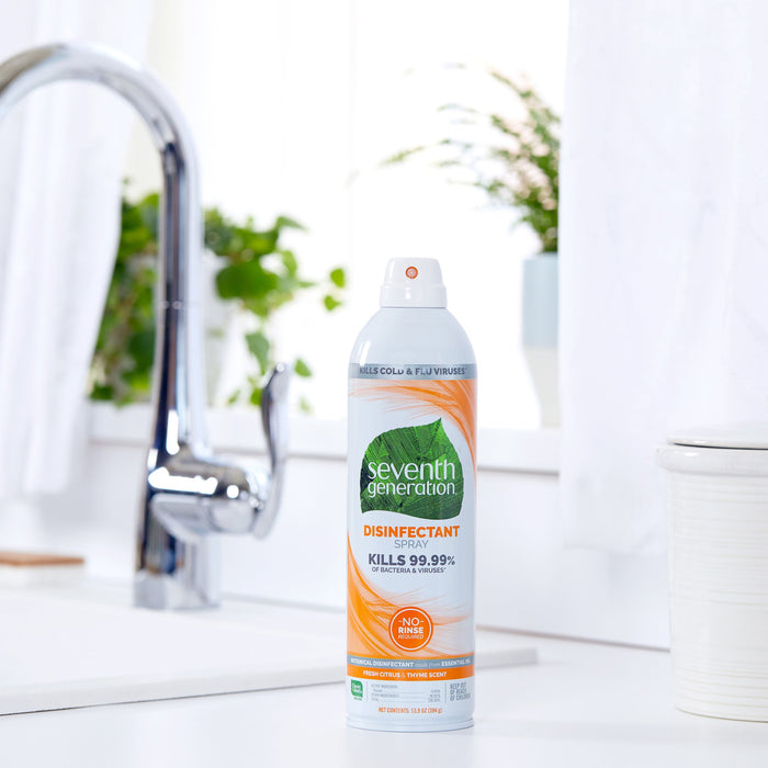 A can of Seventh Generation Disinfectant Spray sits on a kitchen counter near a stainless steel faucet, ready to eliminate germs on nonporous surfaces, with plants in the background.